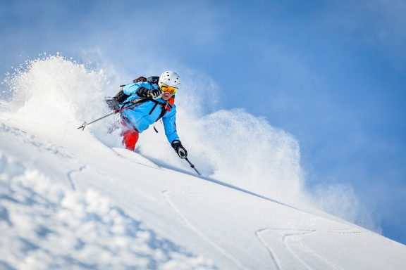 Un skieur descente sur une pente enneigée avec de la neige qui s'envole.
