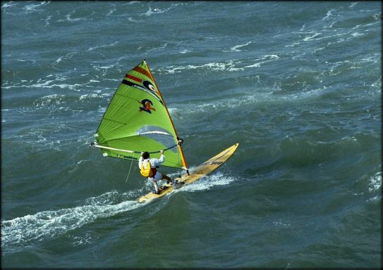 Un windsurfer navigue sur des eaux agitées avec une voile verte.